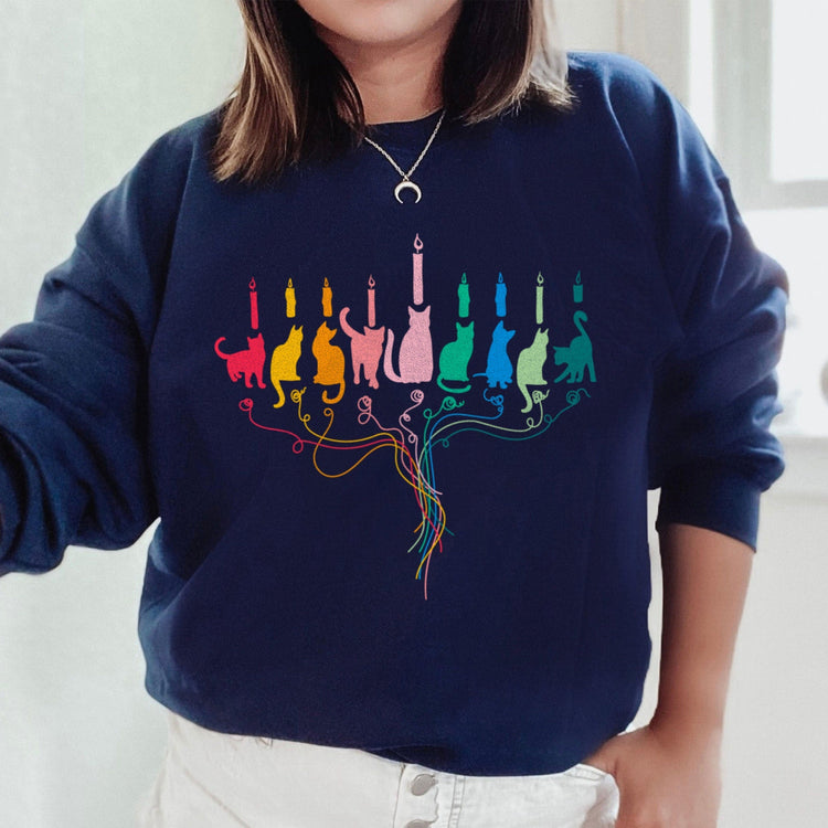 A person wearing a navy blue sweatshirt with a colorful graphic of cats menorah on the front.
